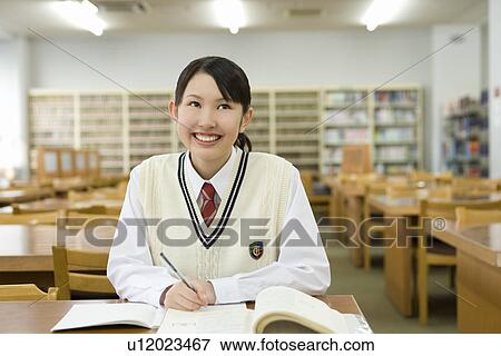 Stock Photo - Portrait of a teenage girl studying in library, smiling and looking up. Fotosearch