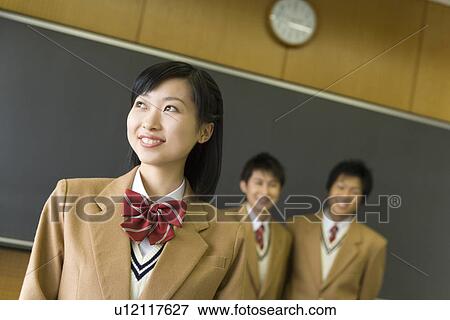 Stock Photo - Portrait of three high school students standing in classroom, smiling. Fotosearch