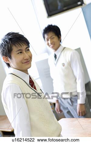 Stock Image - Portrait of two high school students standing in classroom, looking at camera. Fotosearch