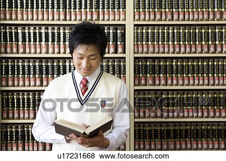 Stock Photo - Teenage boy reading a book in front of bookcase. Fotosearch