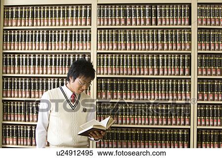 Stock Photography - Teenage boy reading a book in front of bookcase. Fotosearch