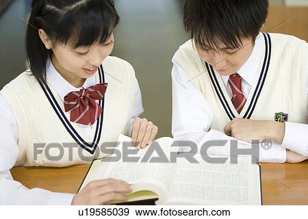 Stock Photo - Teenage couple reading a book in library, smiling. Fotosearch