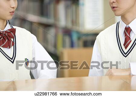 Stock Photograph - Teenage couple sitting at table and talking in library. Fotosearch