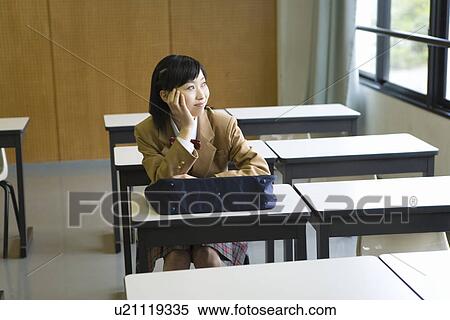 Stock Photography - Teenage girl smiling and sitting at desk in classroom, resting chin in hand. Fotosearch