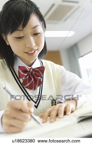 Stock Image - Teenage girl studying at desk in classroom, smiling. Fotosearch