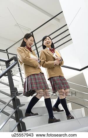 Stock Image - Teenage girls holding text books and walking down the stairs, smiling. Fotosearch