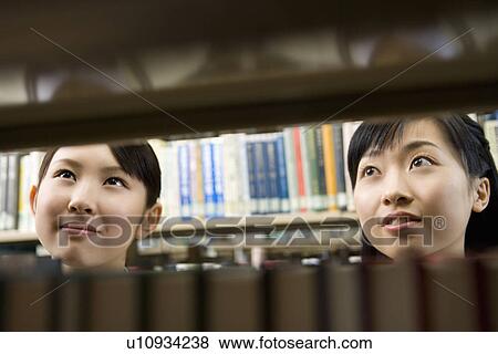 Stock Photo - Teenage girls smiling and standing between bookcases. Fotosearch