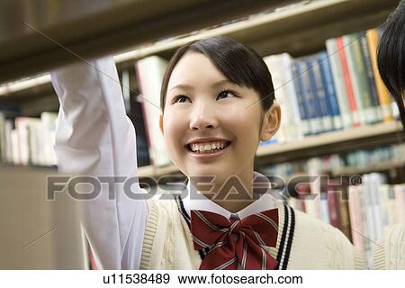 Stock Photo - Teenage girls smiling and standing between bookcases. Fotosearch