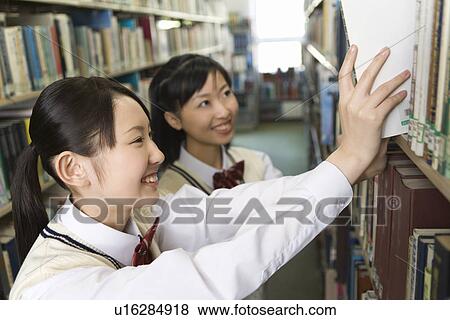 Stock Photo - Teenage girls smiling and standing between bookcases. Fotosearch