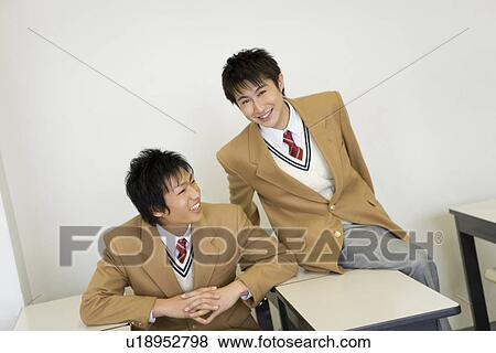 Stock Photo - Two teenage boys sitting at desk and talking in classroom, portrait for one. Fotosearch