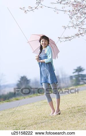 Stock Image - Portrait of a woman holding an umbrella, smiling and looking at camera, front view, Japan. Fotosearch