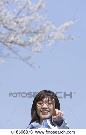 Portrait of a woman pointing forward and standing under the cherry tree, smiling and looking at camera, front view, blue background, Japan View Large Photo Image Stock Image - Portrait of a woman pointing forward and standing under the cherry tree, smiling and looking at camera, front view, blue background, Japan. Fotosearch