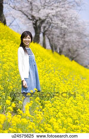 Stock Photography - Portrait of a woman standing in rape field, smiling and looking at camera, side view, Japan. Fotosearch