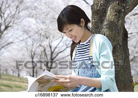 Stock Photo - Woman reading a magazine under the cherry tree, side view, Japan. Fotosearch