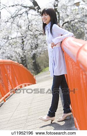 Stock Photograph - Young Woman Leaning on a Rail, Side View, Differential Focus. Fotosearch