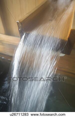 Stock Image - Hot water running out from wooden tap, hot spring, high angle view, close up, Japan. Fotosearch