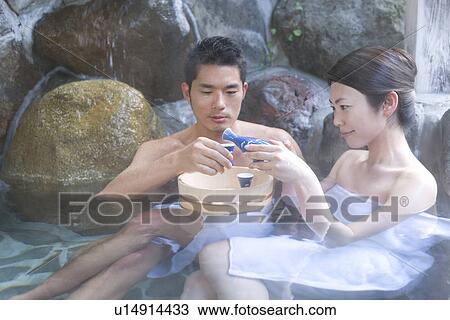 Stock Image - Japanese couple enjoying Sake in a hot tub, front view, side view, Japan. Fotosearch