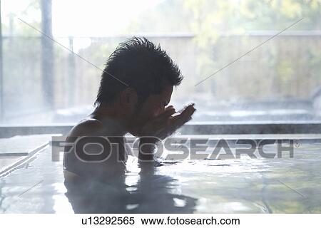 Stock Photography - Man in a hot tub splashing hot water on face, side view, blurred motion, Japan. Fotosearch