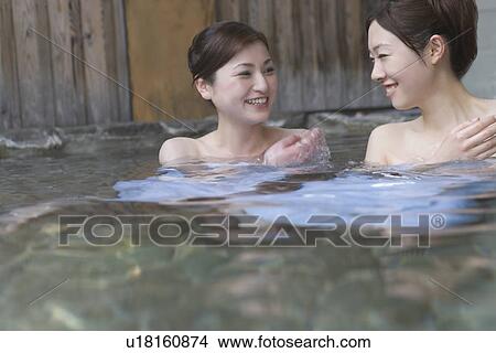 Picture - Two women in hot tub, smiling, front view, Japan. Fotosearch