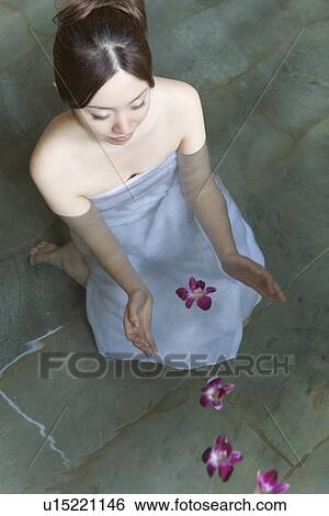 Stock Photograph - Woman floating flower heads on the hot tub, high angle view, Japan. Fotosearch