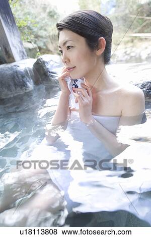 Stock Photo - Woman in a hot tub, holding a towel, side view, Japan. Fotosearch