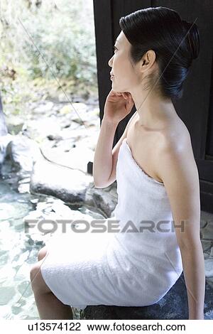 Stock Image - Woman in towel soaking her legs in a hot tub, side view, Japan. Fotosearch