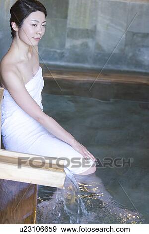Stock Photo - Woman in towel soaking her legs in a hot tub, side view, Japan. Fotosearch