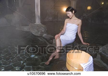 Stock Photograph - Woman in towel soaking her legs in a hot tub, sitting crossed leg at knee, front view, Japan. Fotosearch