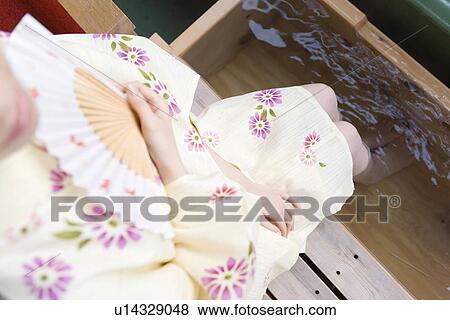 Stock Photo - Woman in Yukata soaking her legs in the footbath, holding a Japanese folding fan, high angle view, Japan. Fotosearch