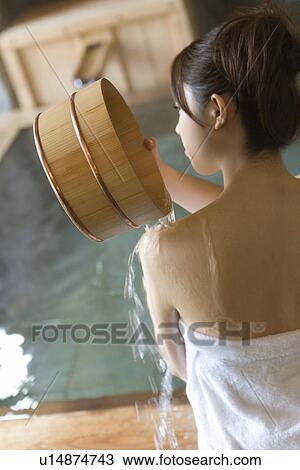 Stock Image - Woman pouring water on her shoulder with wooden tub, rear view, Japan. Fotosearch