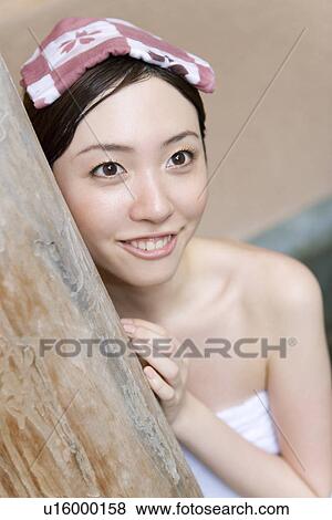 Stock Photo - Woman putting a towel on her head in hot tub, front view, Japan. Fotosearch