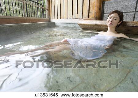 Stock Photography - Woman relaxing in hot tub, closing eyes, front view, Japan. Fotosearch