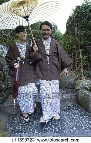 Stock Image - Mature Adult Couple Going Down the Stairs with Sharing a Paper Umbrella, Front View, Full Length, Low Angle View. Fotosearch