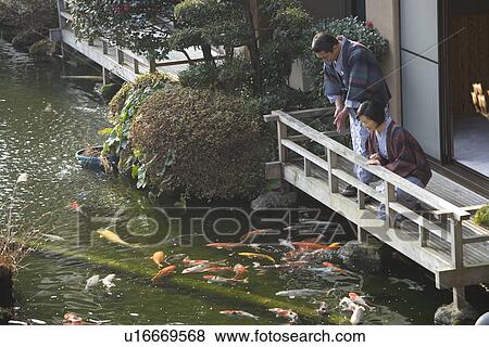 Stock Photo - Mature Adult Couple Looking at Carp from the Wooden Balcony, Side View, High Angle View, Three Quarter Length. Fotosearch