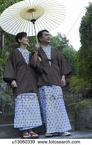 Stock Photo - Mature Adult Couple Sharing a Paper Umbrella and Looking Away, Front View, Full Length, Low Angle View. Fotosearch