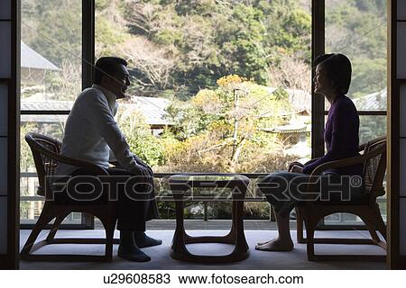 Stock Image - Mature Adult Couple Sitting By the Window, Silhouette, Side View, Full Length. Fotosearch