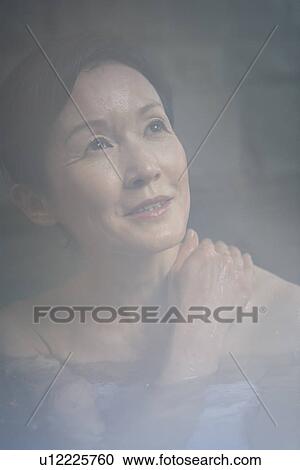 Stock Image - Mature Adult Woman Soaking in a Hot Spring Bath, Front View, Head and Shoulder, Close Up. Fotosearch