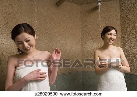 Stock Image - Two women standing under the hot taps, hot water dropping, front view, Japan. Fotosearch