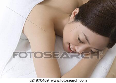 Stock Photo - Woman lying on bed in beauty salon, closing eyes, high angle view, Japan. Fotosearch