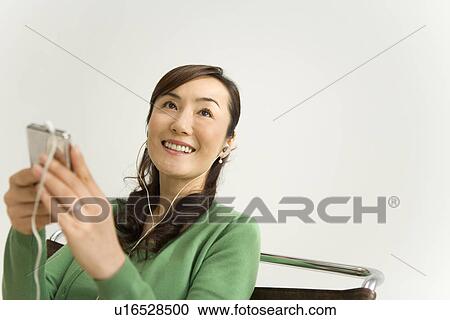 Stock Image - A Mature Adult Woman Listening to Music with a Portable Music Player, Low Angle View, Differential Focus, Copy Space. Fotosearch