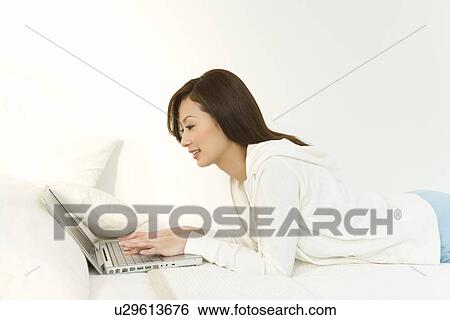 A woman lying on a bed and using a laptop, side view, white background View Large Photo Image Stock Photograph - A woman lying on a bed and using a laptop, side view, white background. Fotosearch