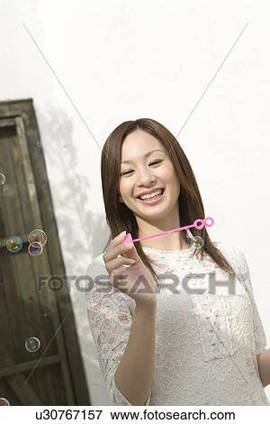 Stock Photo - A woman smiling and holding a bubble wand, front view, white background. Fotosearch