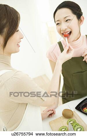Picture - One woman feeding to the other in the kitchen, front view, side view. Fotosearch