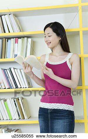 Stock Photography - Portrait of a Young Woman Reading a Book, Smiling, Front View. Fotosearch