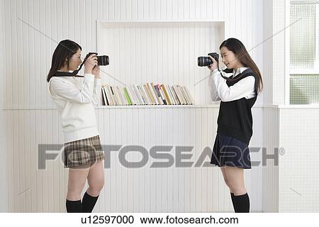Stock Image - Twin sisters holding cameras and photographing each other, side view. Fotosearch