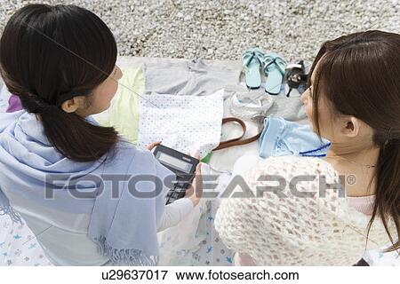 Stock Photo - Two women sitting at a flea market, one holding a calculator, high angle view, rear view. Fotosearch
