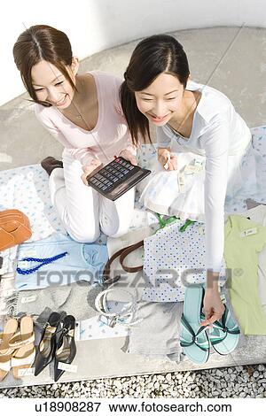 Stock Photo - Two women smiling and selling their stuff at a flea market, one holding a calculator, high angle view. Fotosearch