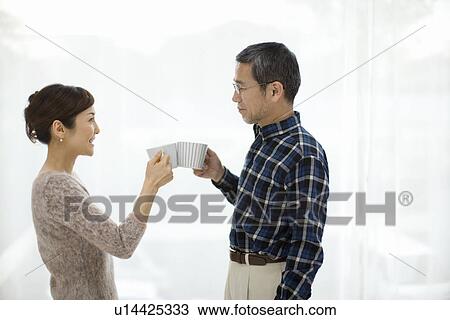 Stock Image - A Mature Adult Couple Toasting with Coffee Cups, Side View. Fotosearch
