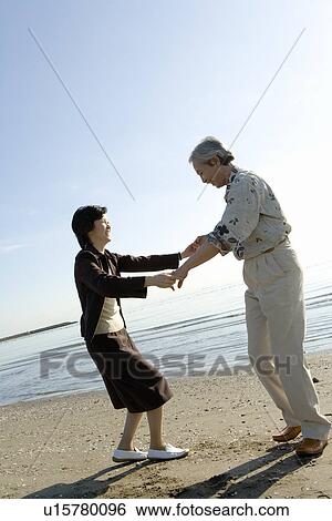 Stock Photograph - A Mature Couple Enjoying on the Beach, Side View, Full Length. Fotosearch