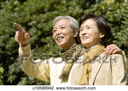 Stock Image - A Mature Couple Nestling Close to Each Other and Looking Away, Head and Shoulder, Low Angle View. Fotosearch